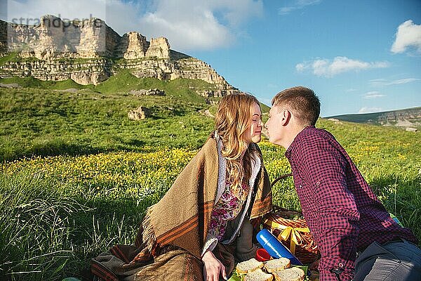 Junges Ehepaar küsst sich beim Picknick im Freien bei Sonnenuntergang. Das Konzept einer glücklichen jungen Familie und Einheit mit der Natur
