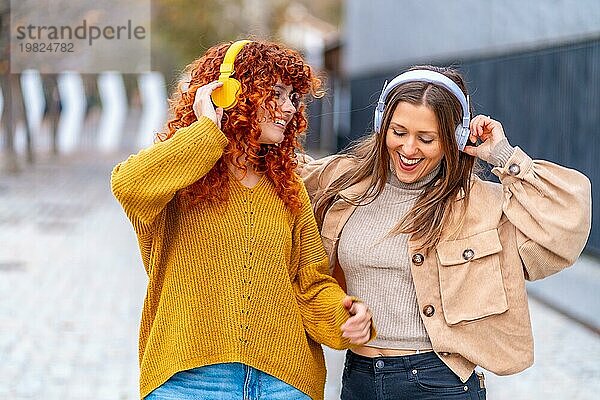 Frontalansicht von zwei glücklichen Frauen  die auf der Straße tanzen und Musik hören