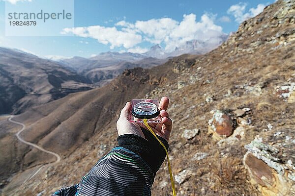 Ein Mann hält einen Taschenmagnetkompass zur Navigation vor dem Hintergrund eines felsigen Abhangs und epischer Felsen unter einem blaün Himmel und weißen Wolken. Das Konzept  einen Weg zu finden. Freiheit erlangen. Freiheit der Wahl
