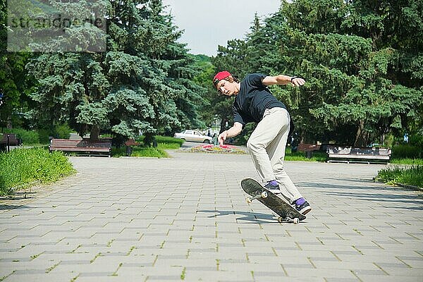 Langhaariger Skater Teenager in TShirt und Turnschuhmütze springt den Ollie vor dem Hintergrund eines stürmischen Himmels über der Stadt