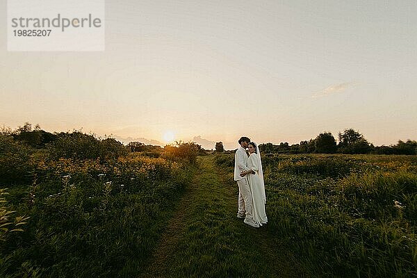 Verliebtes Brautpaar bei Sonnenuntergang auf dem Feld  die Braut und der Bräutigam in weißer Hochzeit