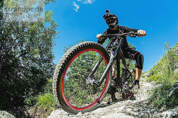 Ein junger Fahrer auf einem Fahrrad für Downhill steigt die Felsen im Wald hinunter