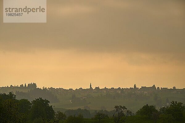 Silhouette eines Dorfes auf Hügel unter einem orangefarbenen Himmel beim Sonnenaufgang  Hirzel  Horgen  Voralpen  Kanton Zürich  Schweiz  Europa