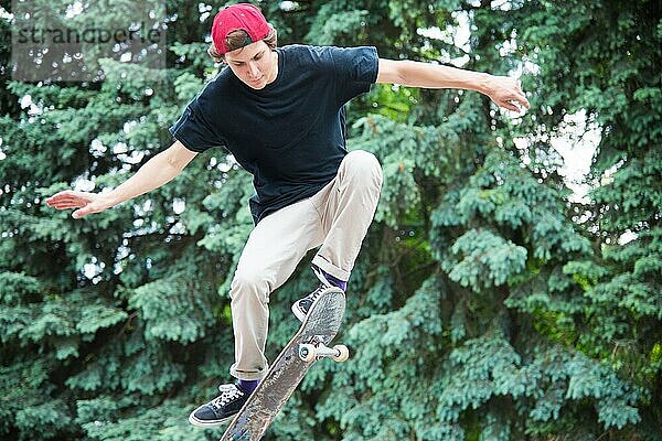 Langhaariger Skater Teenager in TShirt und Turnschuhmütze springt den Ollie vor dem Hintergrund eines stürmischen Himmels über der Stadt