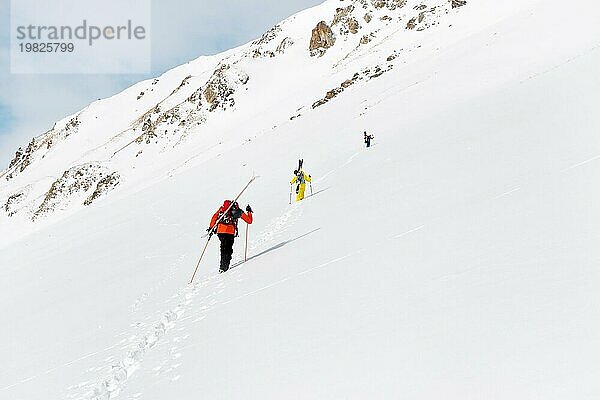 Zwei Ski Freerider klettern den Hang im Tiefschnee hinauf  die Ausrüstung auf dem Rücken am Rucksack befestigt. Das Konzept des Winter Extremsports