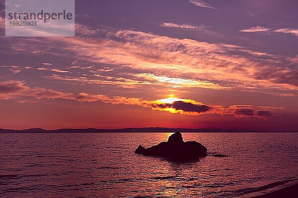 Lila Sonnenuntergang über dem Meer in Griechenland Küste mit Wolken und Stein Silhouette