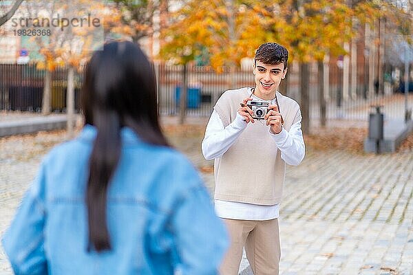 Junger Mann  der ein Foto mit einer Digitalkamera für einen Freund in der Stadt macht