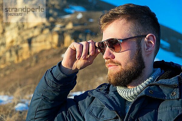 Porträt von Streng und ernst Hipster Reisenden mit einem Bart Halten Sie Sonnenbrille mit den Fingern in der Natur. Reisen Lifestyle Abenteuer Outdoor Erholung Outdoor Sport Tracking