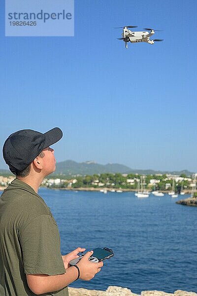 Glücklicher Teenager  fliegende Drohne an der Mittelmeerküste  gegen blauen Himmel an einem sonnigen Tag Spanien  Balearen