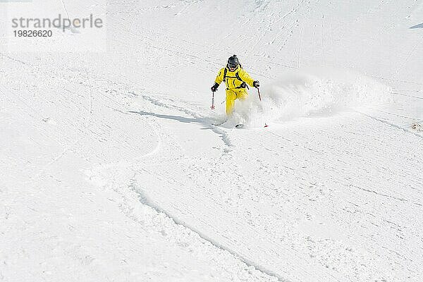 Ein männlicher Freerider mit Bart fährt im Backcountry mit hoher Geschwindigkeit von der Piste ab und hinterlässt eine Spur aus Pulverschnee. Das Konzept der Freeride Kultur und der Backcountry Destinationen im extremen Skisport