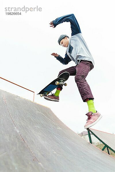 Der Teenager Skateboarder in der Mütze macht einen Trick mit einem Sprung auf der Rampe im Skatepark. Isolierte Skater und Rampe auf weißem Hintergrund