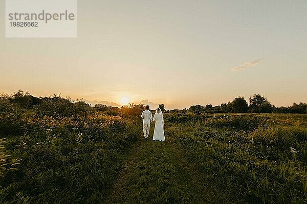 Verliebtes Brautpaar bei Sonnenuntergang auf dem Feld  die Braut und der Bräutigam in weißer Hochzeit