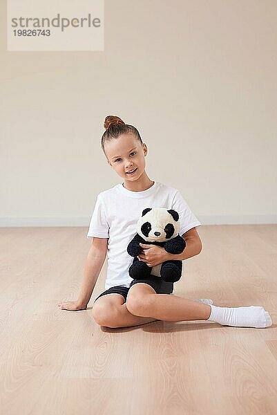 Nettes Mädchen Kind posiert im Studio mit einem Stofftier in einem hellen Studio. Das Konzept der Bildung  Tanz  Sport  Pilates  Stretching  gesunden Lebensstil. Gemischte Medien