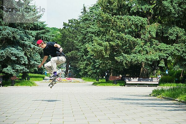 Langhaariger Skater Teenager in TShirt und Turnschuhmütze springt den Ollie vor dem Hintergrund eines stürmischen Himmels über der Stadt