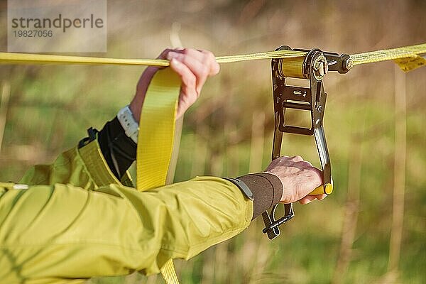 Nahaufnahme Hände eines Mannes  der die Slacklining Ausrüstung einstellt  bevor er verrückte Slacklining Tricks vorführt und auf einer Slackline in einem Park in der Natur läuft