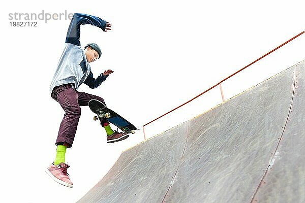 Der Teenager Skateboarder in der Mütze macht einen Trick mit einem Sprung auf der Rampe im Skatepark. Isolierte Skater und Rampe auf weißem Hintergrund