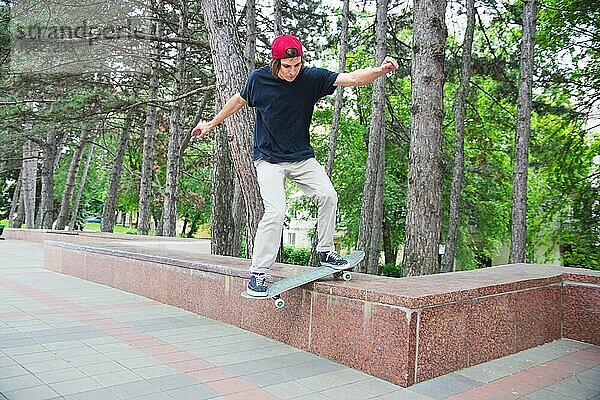 Langhaariger Skater Teenager in TShirt und Turnschuhmütze springt den Ollie vor dem Hintergrund eines stürmischen Himmels über der Stadt