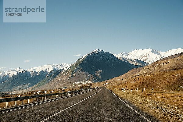 Blick auf die Herbststraße  die in die Berge zu den schneebedeckten Gipfeln des Kaukasus führt. Das Konzept  mit dem Auto in die Berge zu fahren