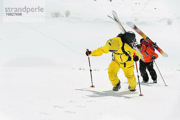 Zwei Ski Freerider klettern den Hang im Tiefschnee hinauf  die Ausrüstung auf dem Rücken am Rucksack befestigt. Das Konzept des Winter Extremsports