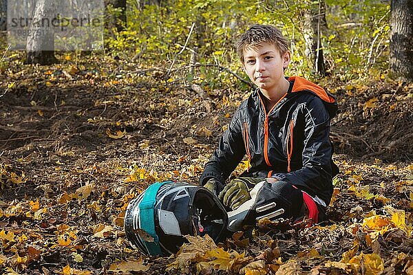 Porträt eines jungen Motorradfahrers  der im Wald auf einem gelben Laubdach sitzt und einen Integralhelm trägt. Das Konzept der Outdoor Sportarten für Kinder