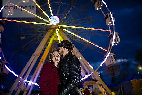Verliebtes Paar in einem Vergnügungspark in der Nähe eines Riesenrads bei einer Verabredung bei kaltem Wetter. Das Konzept von Liebe und Freude in Beziehungen