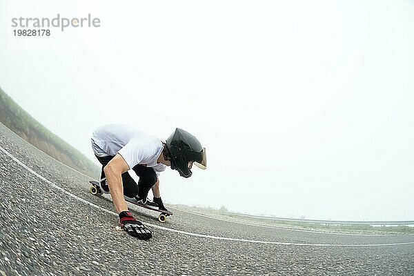 Ein junger Mann in einem Vollvisierhelm auf einer Landstraße in einer Rutsche passiert eine Kurve vor dem Hintergrund von niedrigen Wolken und Nebel