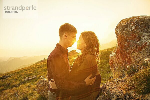 Junges glückliches Paar küsst sich in der Natur gegen die untergehende Sonne bei Sonnenuntergang. Das Konzept einer glücklichen jungen Familie und die Kommunikation der Jugend mit der Natur