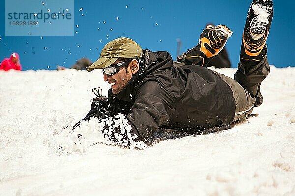 Training zur Korrektur des Ausrutschens auf einer Piste oder einem Gletscher mit Hilfe eines Eispickels. Ein voll ausgerüsteter Rucksacktourist rutscht auf dem Bauch einen verschneiten Hang im Gebirge entlang  wobei das Gleiten durch einen Eispickel behindert wird. Ausbildung eines unerfahrenen Bergsteigers vor der Besteigung eines Berges