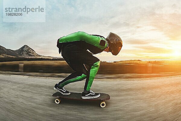 Ein junger Mann in einem Fullface Helm und einem Lederanzug in einem speziellen Gestell fährt ein Longboard auf afsaltu Sonnenuntergang im Hintergrund Berge und schönen Himmel mit hoher Geschwindigkeit