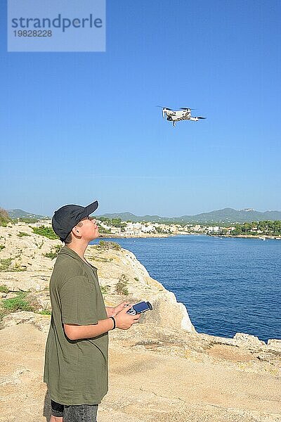 Glücklicher Teenager  fliegende Drohne an der Mittelmeerküste  gegen blauen Himmel an einem sonnigen Tag Spanien  Balearen