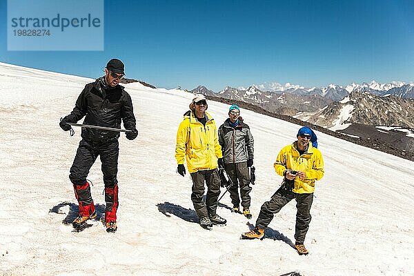 Training zum richtigen Abrutschen an einem Hang oder auf einem Gletscher mit Hilfe eines Eispickels. Ein junger Bergführer mit Bart erklärt seiner Gruppe  wie man das Abrutschen am Hang mit Hilfe eines Eispickels richtig bremst. Vorbereitung vor dem Aufstieg auf den Berggipfel