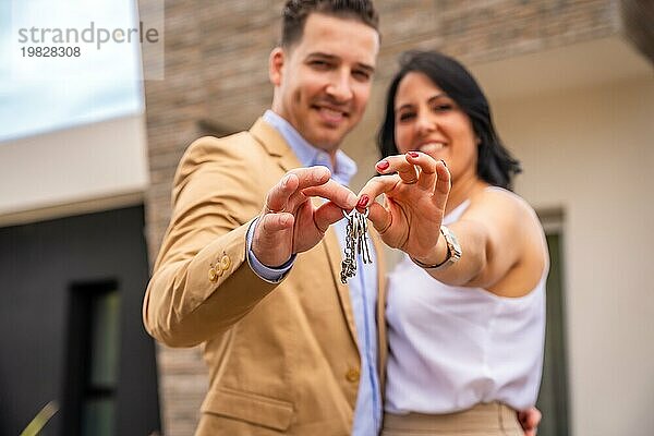Frontalaufnahme eines glücklichen Paares  das die Schlüssel für ein neues Haus zeigt