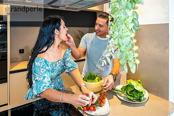 Romantische Szene eines Mannes  der sein Paar mit Kirschen füttert  während er einen schönen Salat im neuen Haus zubereitet