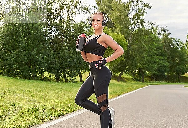 Mädchen posiert mit einem Shaker für Sporternährung im Park. Das Konzept eines gesunden Lebensstils. Sportgeräte. Werbung im Fitness Stil. Gemischte Medien