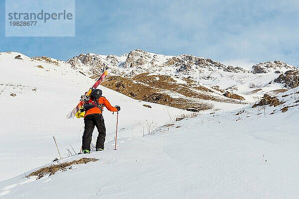 Der Ski Freerider klettert den Hang im Tiefschnee hinauf  wobei die Ausrüstung auf dem Rücken am Rucksack befestigt ist. Das Konzept des Winter Extremsports