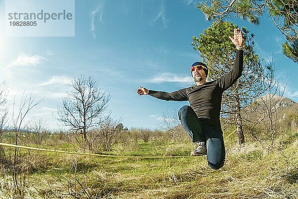 Ein Mann im Alter von auf der Slackline sitzend  das Gleichgewicht haltend und das Leben genießend