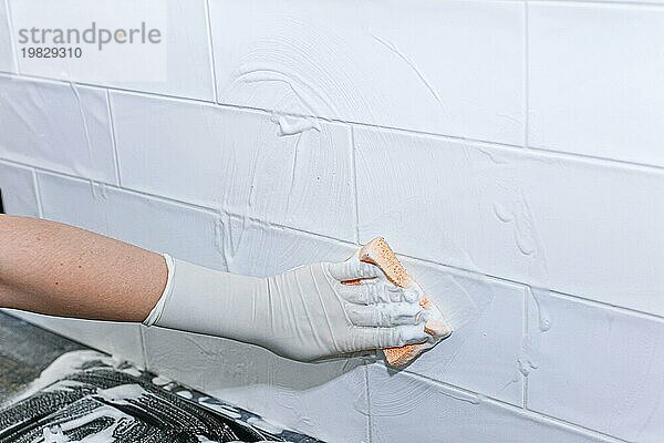 Reinigung von Keramikfliesen zu Hause mit einem Reinigungsmittel in einem Handschuh