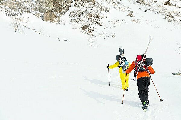 Zwei Ski Freerider klettern den Hang im Tiefschnee hinauf  die Ausrüstung auf dem Rücken am Rucksack befestigt. Das Konzept des Winter Extremsports