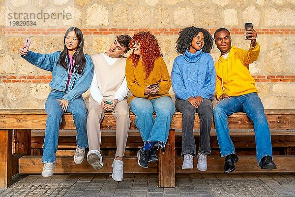 Multiethnische junge Freunde machen Selfies mit dem Handy auf einer Holzbank auf der Straße