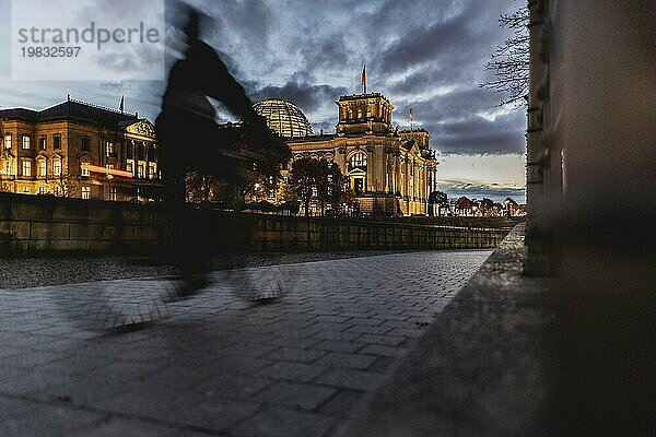 A cyclist in front of the Reichstag stands out at blue hour in Berlin  15.11.2023