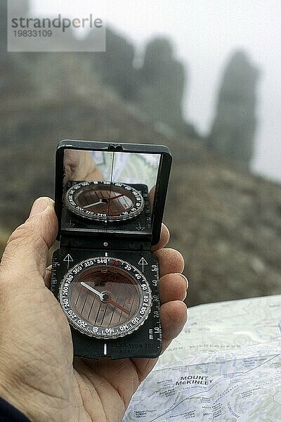 Wanderer liest Kompass und topografische Karte zur Orientierung im Nebel in den Bergen