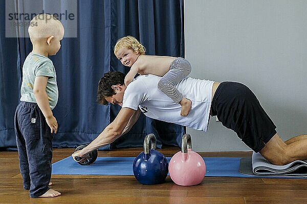 Topic: Young man with a child on his back trains with an abdominal trainer