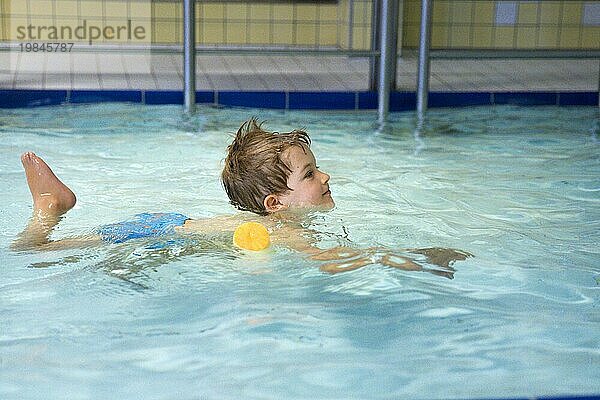 Topic: Preschool child with swimming noodle in swimming pool learns to swim in a public pool
