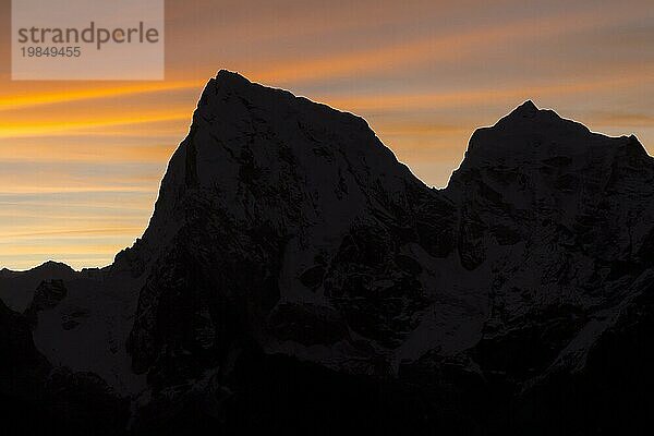 Silhouette der beiden Sechstausender Cholatse und Taboche im Gegenlicht der aufgehenden Sonne  gesehen in der Morgendämmerung an einem Novembertag. Fotografiert vom Gokyo Ri  dem beliebten Trekking Gipfel in der Everest Region. Herbst  Nachmonsun Trekking Saison. Drei Pässe Trek  Khumbu  Everest Region  Himalaya. Sagarmatha Nationalpark  ein UNESCO Weltkulturerbe. Solukhumbu  Nepal  Asien