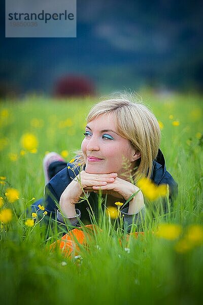 Verträumtes blondes Mädchen liegt im grünen Gras