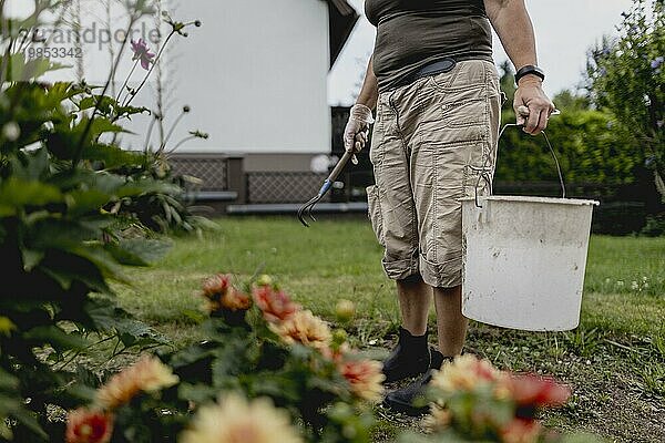Symbolic image on the subject of gardening: A woman stands with a bucket and a rake in a garden in Vierkirchen  18/08/2023