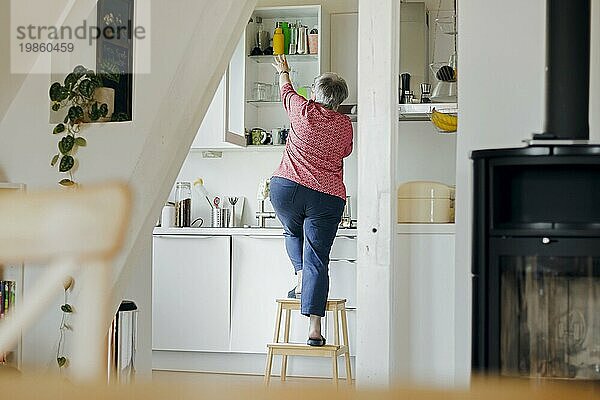 Symbolic photo on the subject of accident risk in the household. An old woman stands on a stool in a kitchen. Berlin  31.08.2023