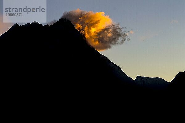 Silhouetten des Siebentausenders Nuptse und des Achttausenders Lhotse  des vierthöchsten Berges der Erde  gekennzeichnet durch orangefarben leuchtende Wolken  gesehen bei Tagesanbruch vom Gokyo Ri  dem beliebten Trekking Gipfel und einem Aussichtspunkt in der Everest Region. Herbst  Nachmonsun Trekking Saison. Gokyo Trek  Khumbu  Everest Region  Himalaya. Sagarmatha Nationalpark  ein UNESCO Weltnaturerbe. Solukhumbu  Nepal  Asien