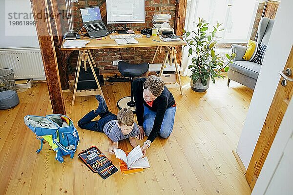 Staged shot: A six-year-old boy lies with his school bag next to his mother's desk and receives help with his homework. Berlin  08/08/2023