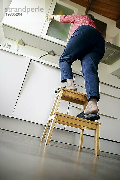 Symbolic photo on the subject of accident risk in the household. An old woman stands on a stool in a kitchen. Berlin  31.08.2023